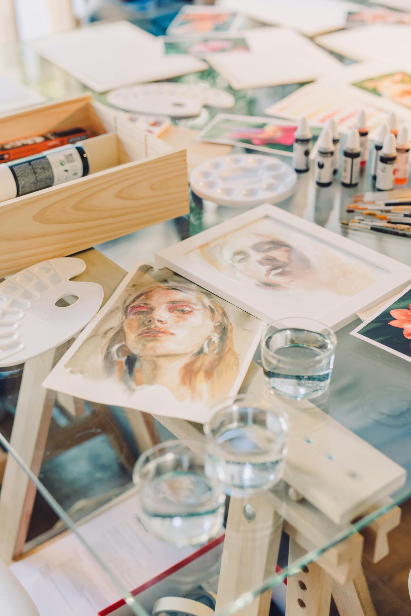 Creative setup of watercolor art supplies with paintings on a glass table.